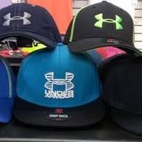 A collection of Under Armour baseball caps in blue, black, and green, stacked on a display shelf.