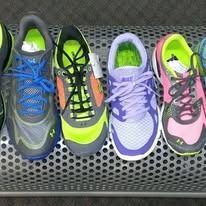 Four pairs of colorful athletic sneakers lined up on a metal, perforated shelf.