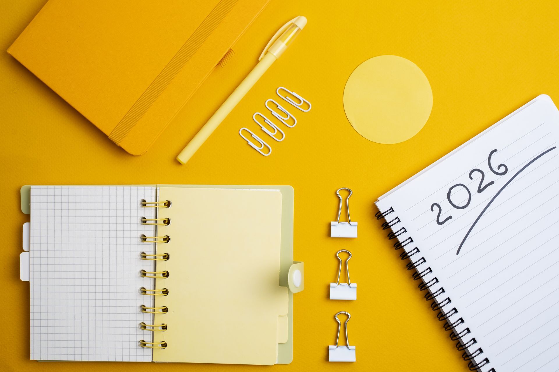 Bright desk-scape of blank 2026 notebooks surrounded by pencils and paperclips