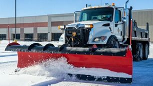Learn More About General Contractors Snowplow truck clearing snow from a parking lot on a sunny day.