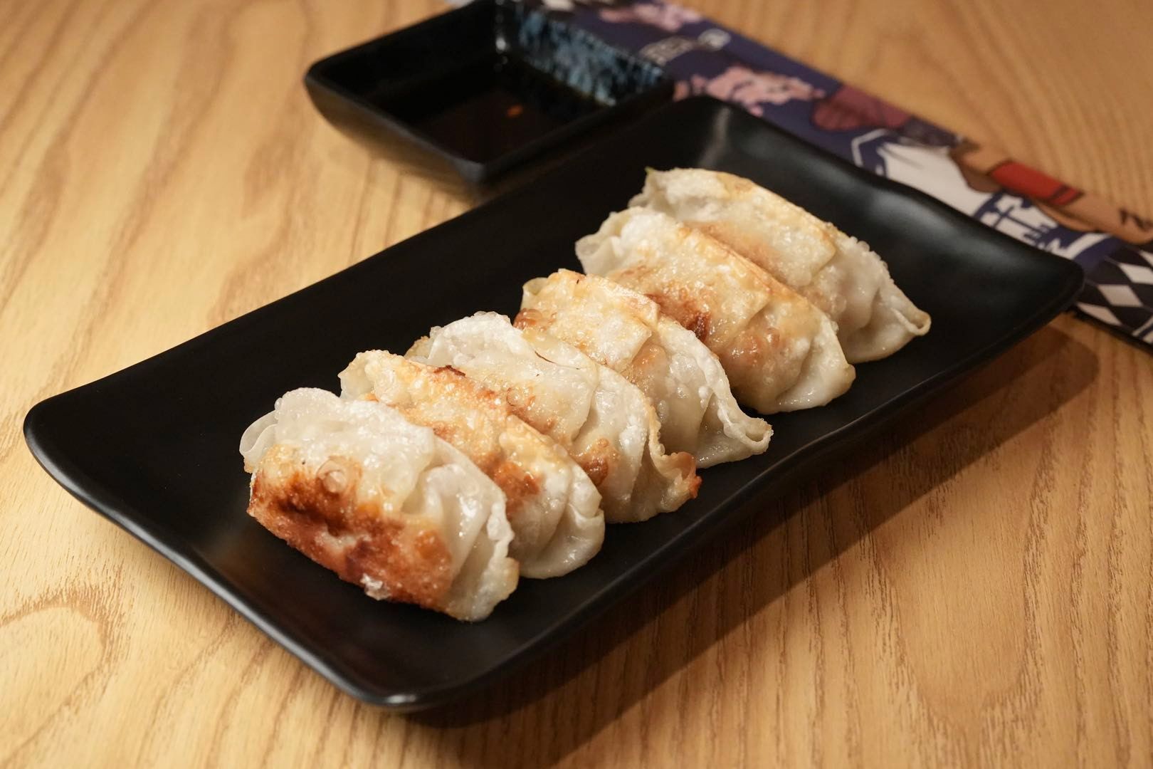 pan-fried Japanese dumplings on a black rectangular plate with dipping sauce and chopsticks