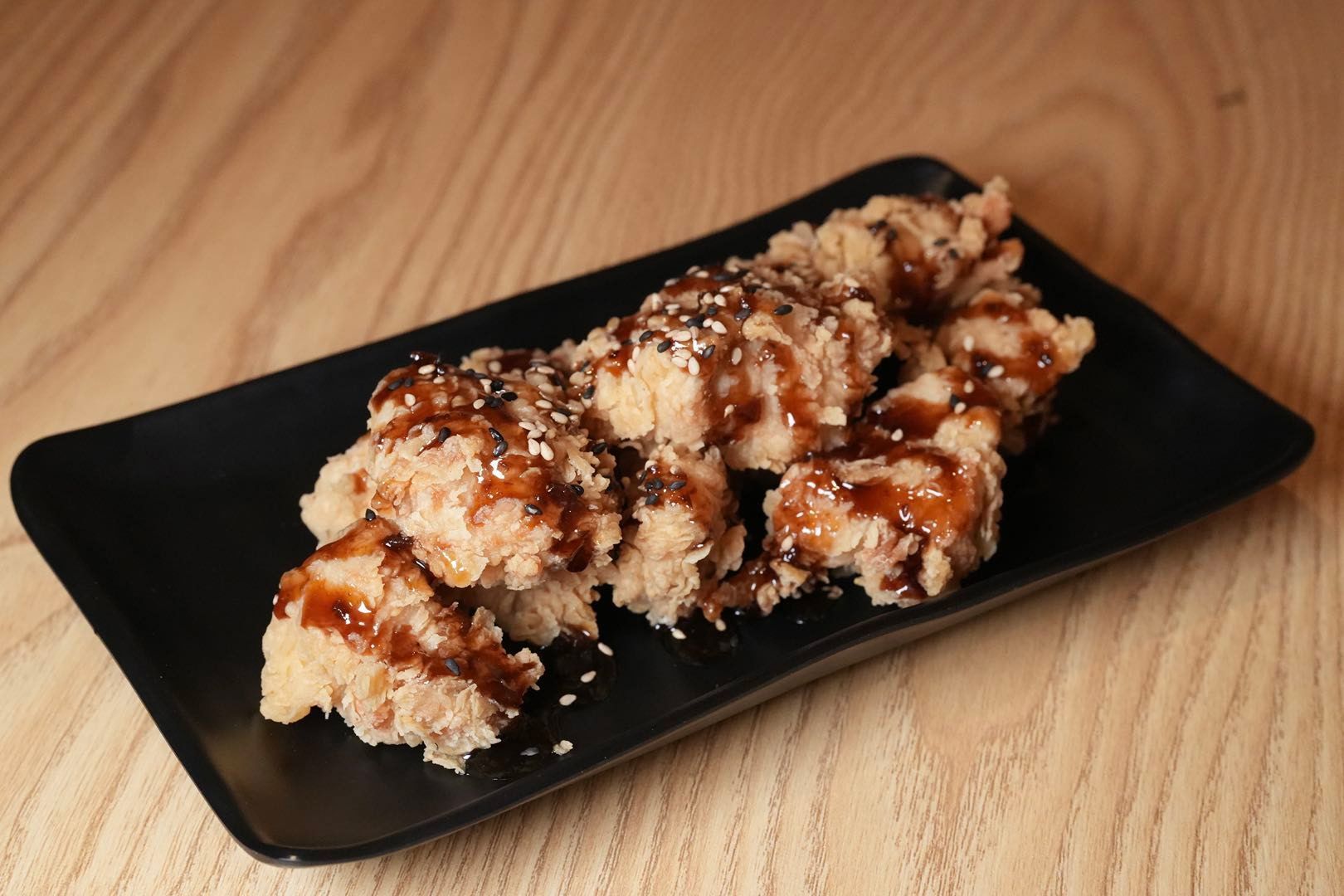 fried chicken pieces with sauce and sesame seeds on a black plate