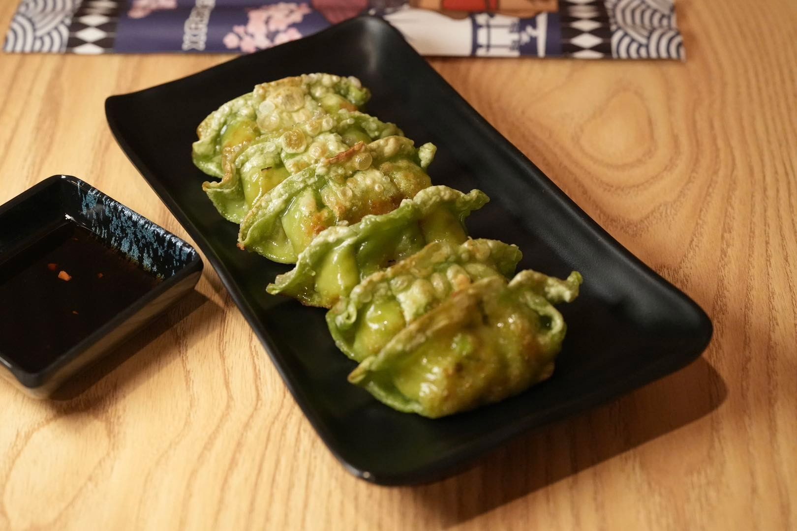green dumplings on a black plate with dipping sauce