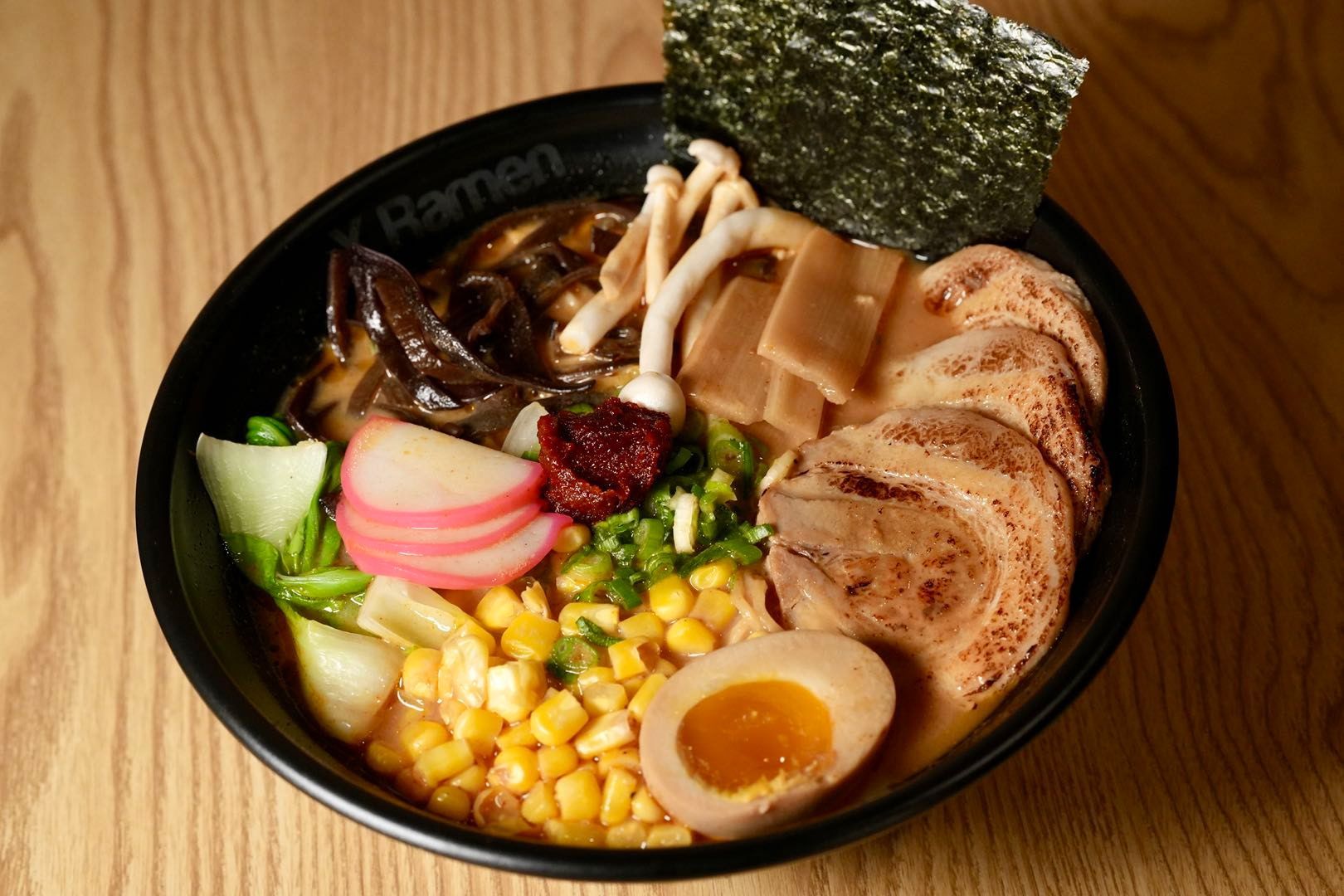 bowl of ramen with various toppings like egg, meat, corn, vegetables, and seaweed