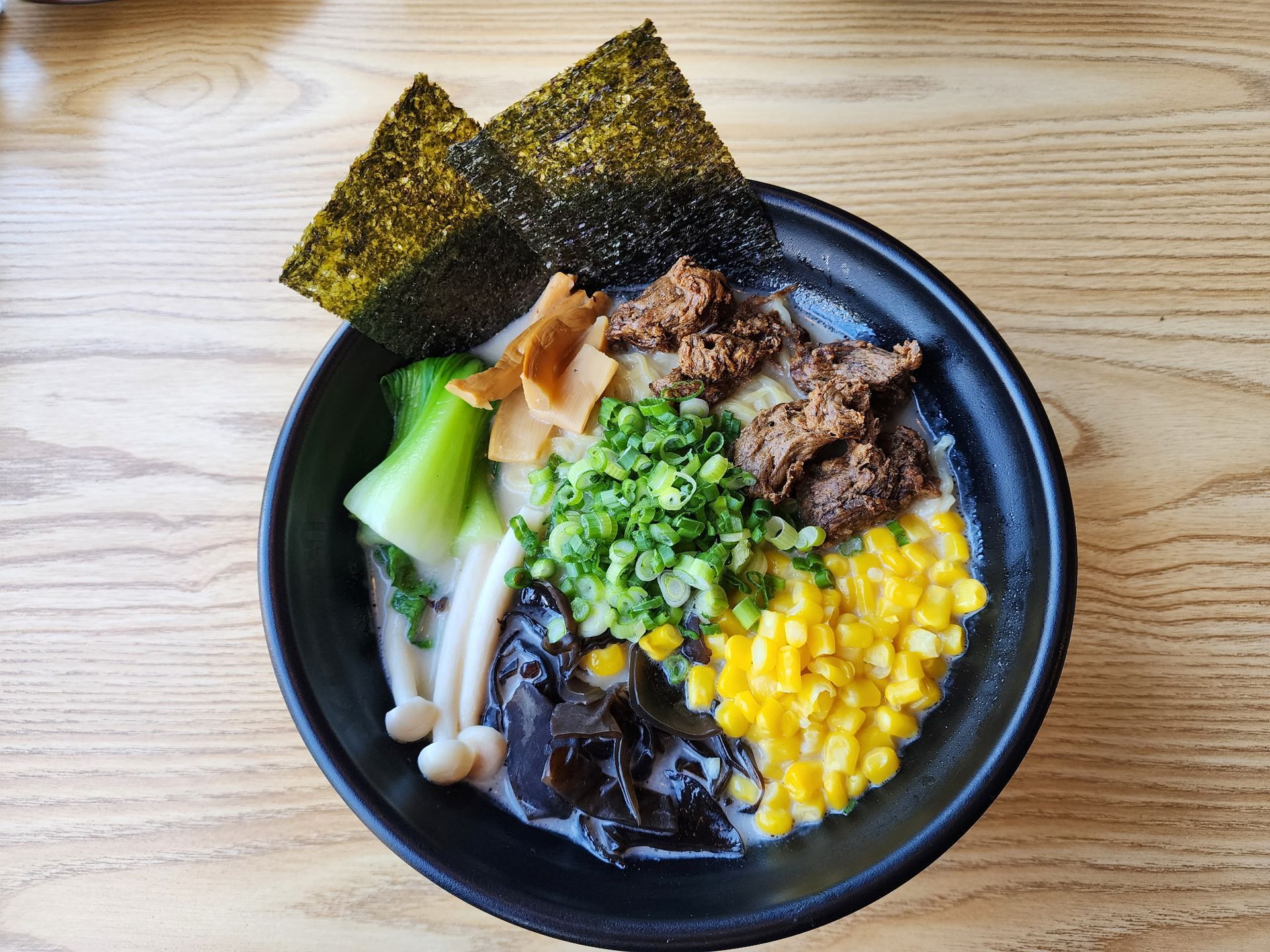 ramen bowl with nori, corn, bok choy, mushrooms, and meat, on a table