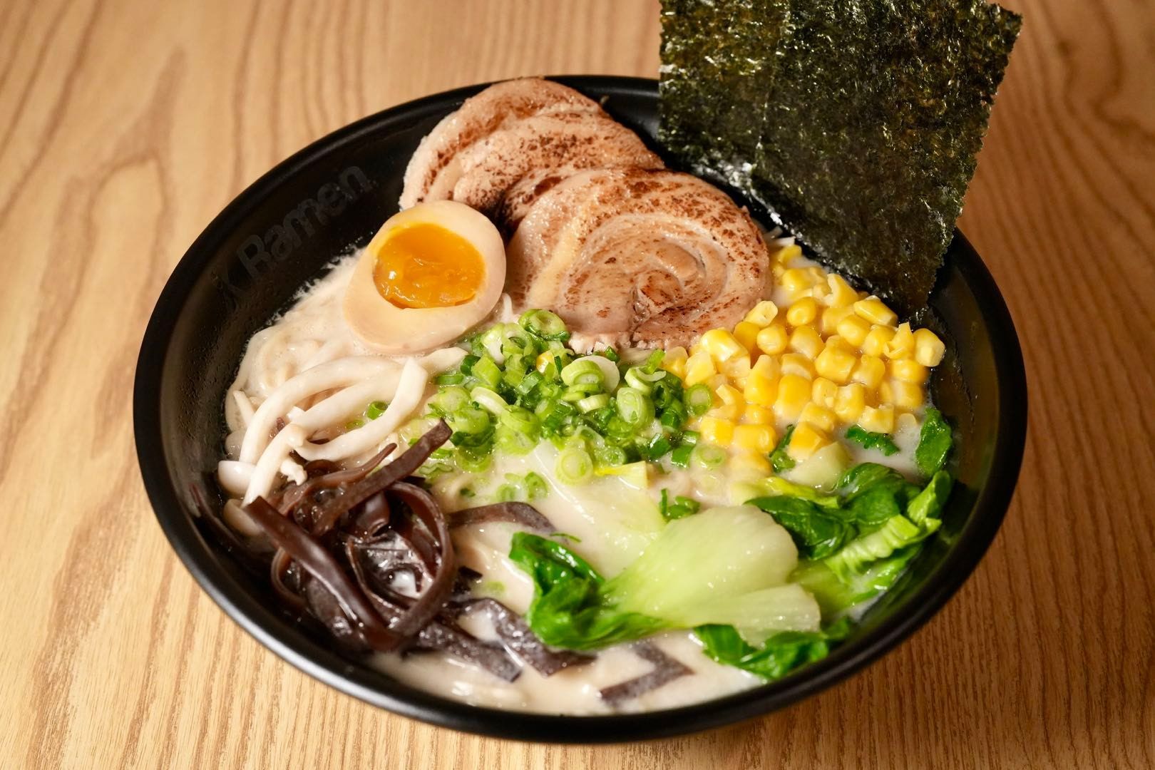 ramen bowl with noodles, pork, egg, corn, seaweed, and vegetables