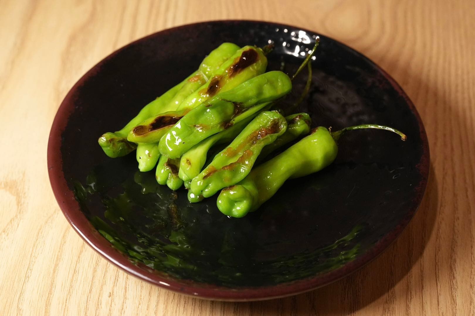 green shishito peppers drizzled with a dark sauce on a dark plate