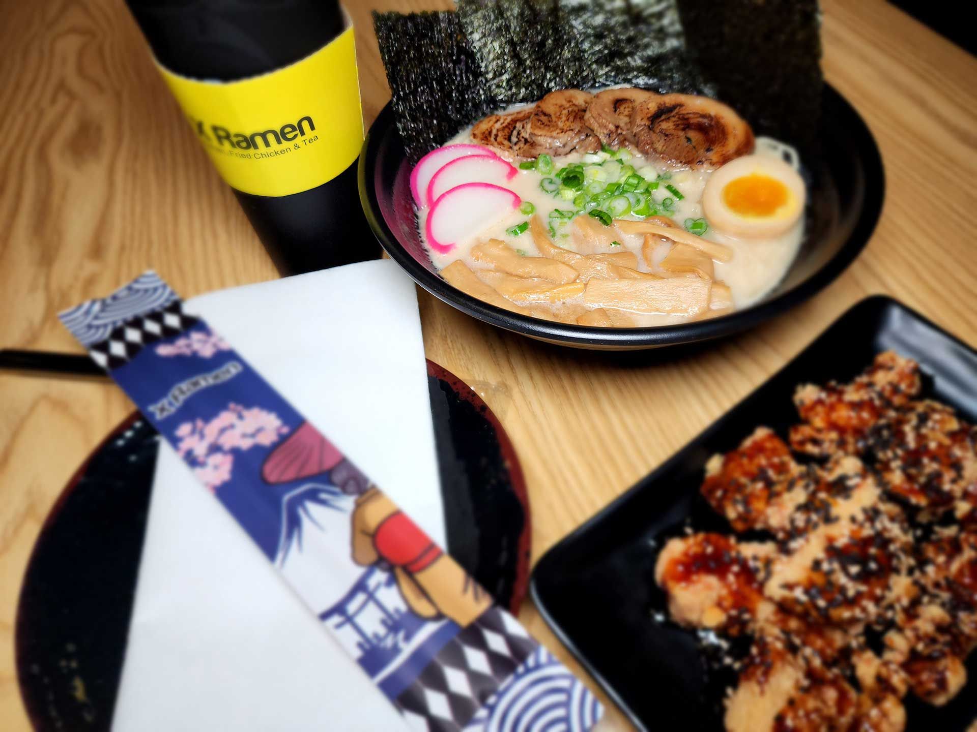 ramen bowl with toppings, fried chicken, chopsticks, a drink, and nori on a table
