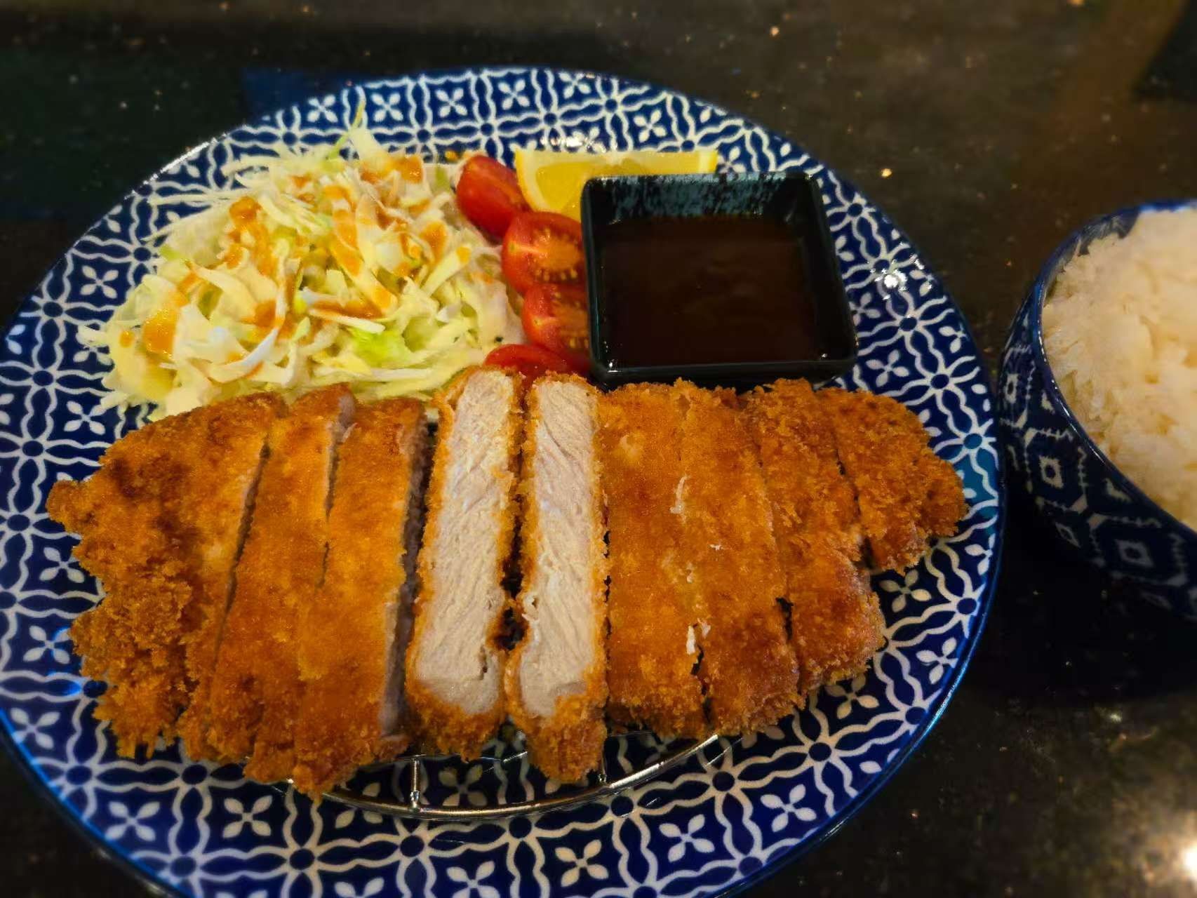 pork cutlet, cabbage salad, dipping sauce, tomatoes, lemon, and rice on a blue patterned plate