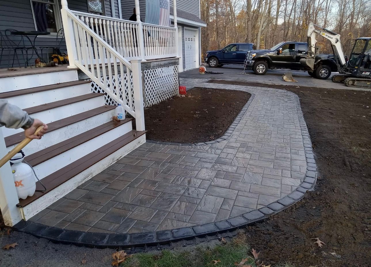 A person is spraying a hose on a sidewalk in front of a house.