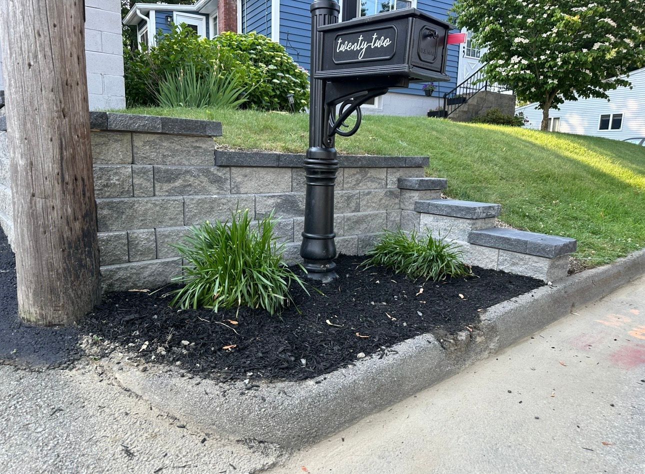 A black mailbox is sitting on the side of the road next to a brick wall.