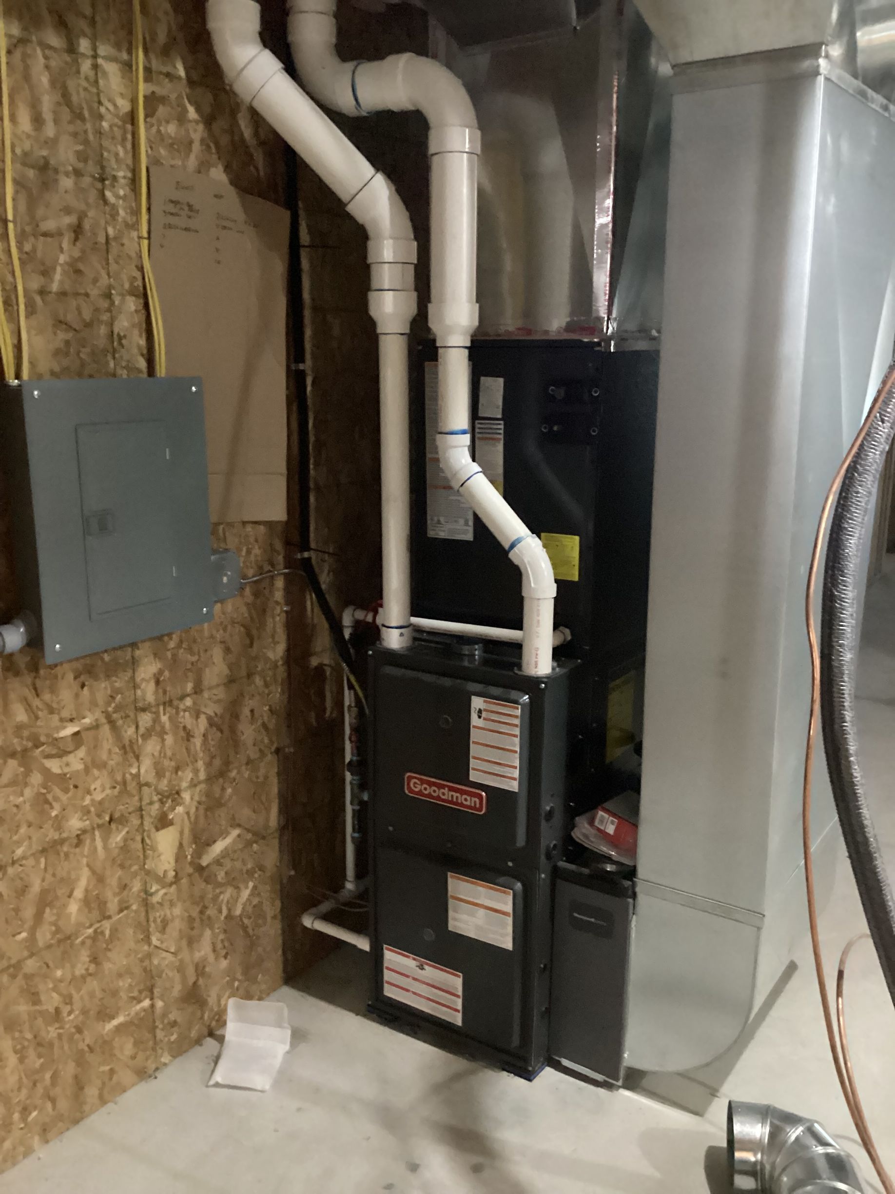 A high-efficiency gas furnace and silver ductwork installed in a utility room with white PVC venting pipes.