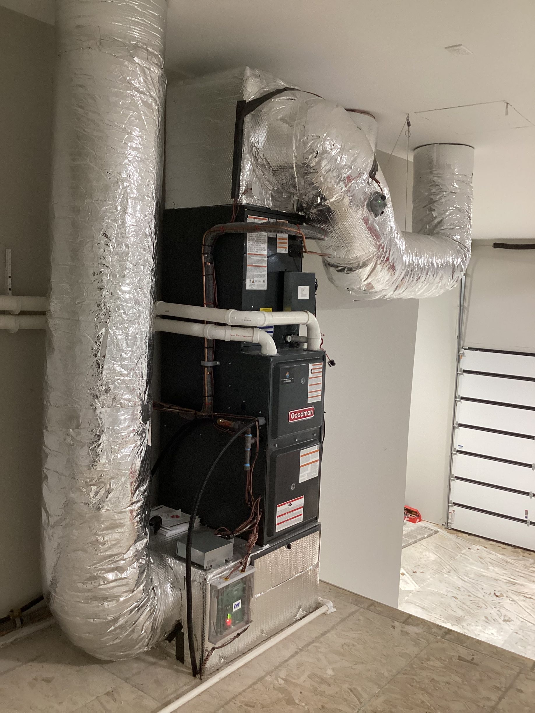 A vertical HVAC unit in a utility room, connected to insulated silver air ducts on a tiled floor.