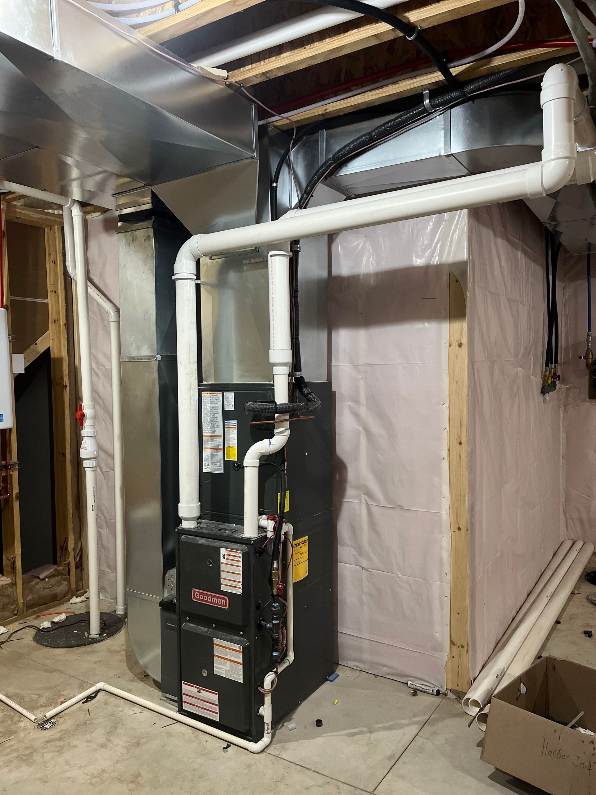A black HVAC furnace unit sits in a basement with white PVC piping connected to its top and sides.