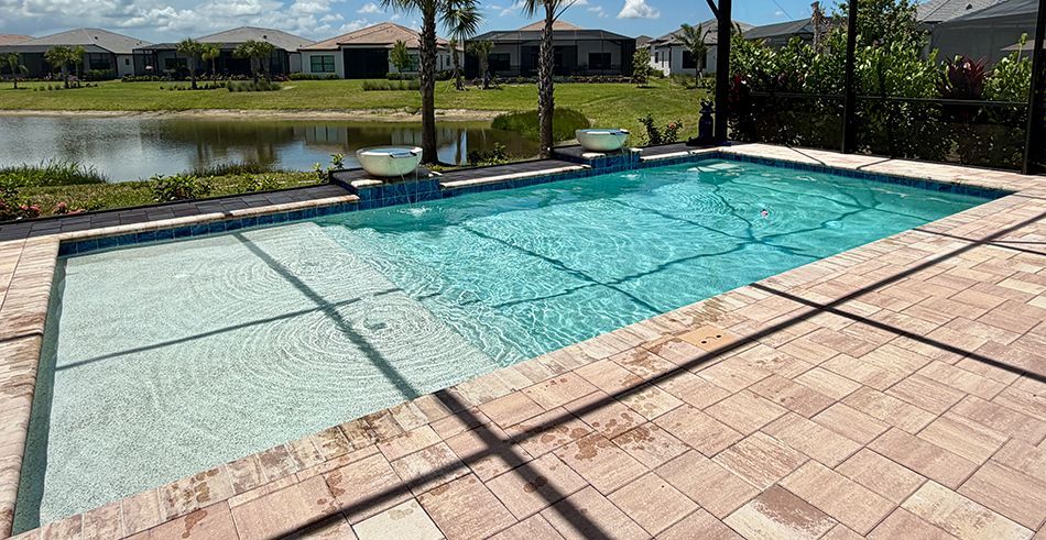 Backyard swimming pool with turquoise water, tan tile deck, and a pond in the background.