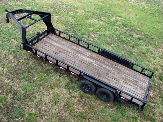 Black utility trailer on grass with wooden deck and black wheels.
