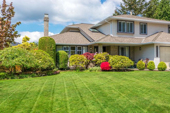House with a well-manicured lawn and colorful shrubs under a blue sky.