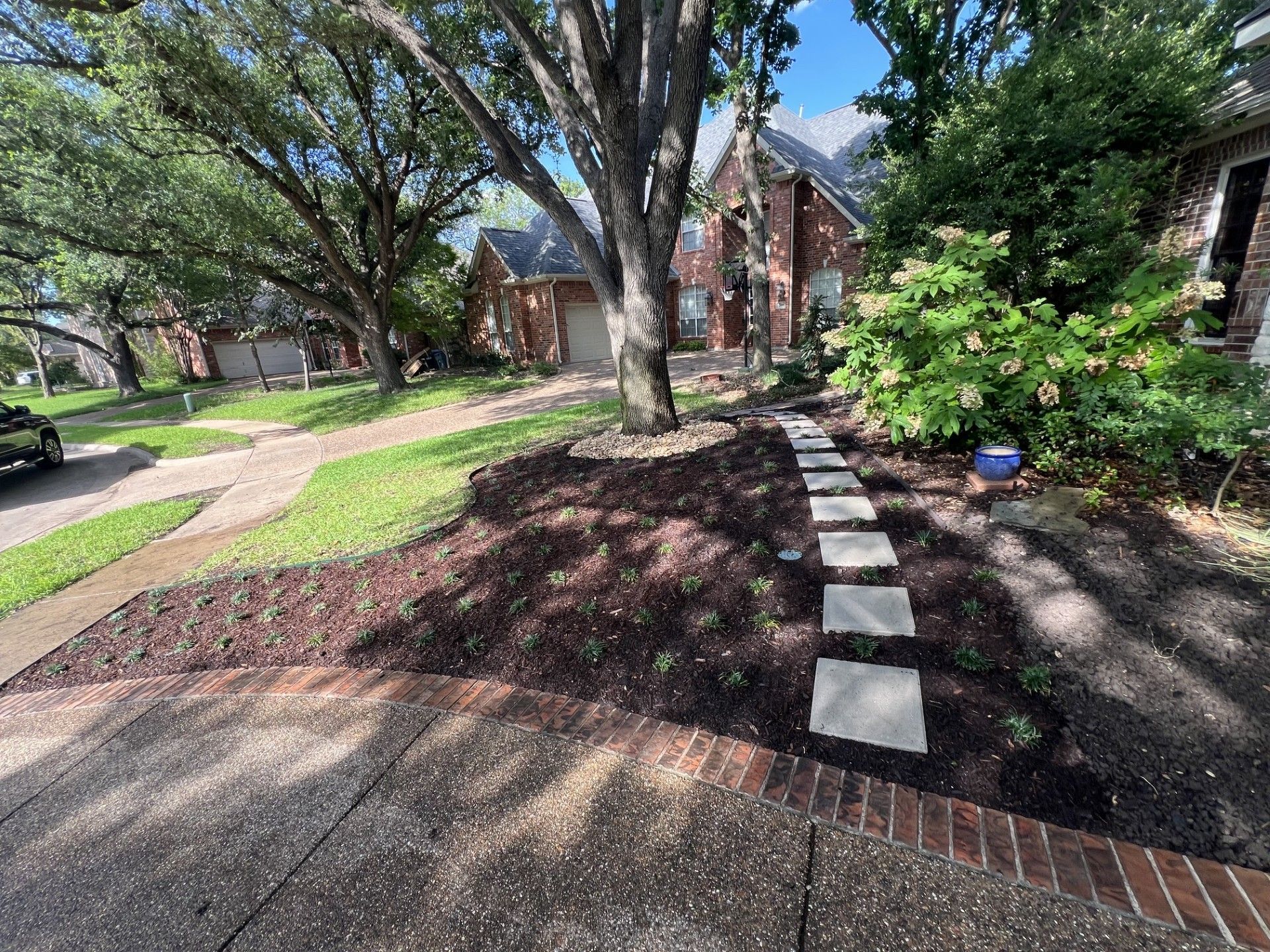 Residential walkway with brick-edged path, stepping stones, and trees in a sunny apartment courtyard