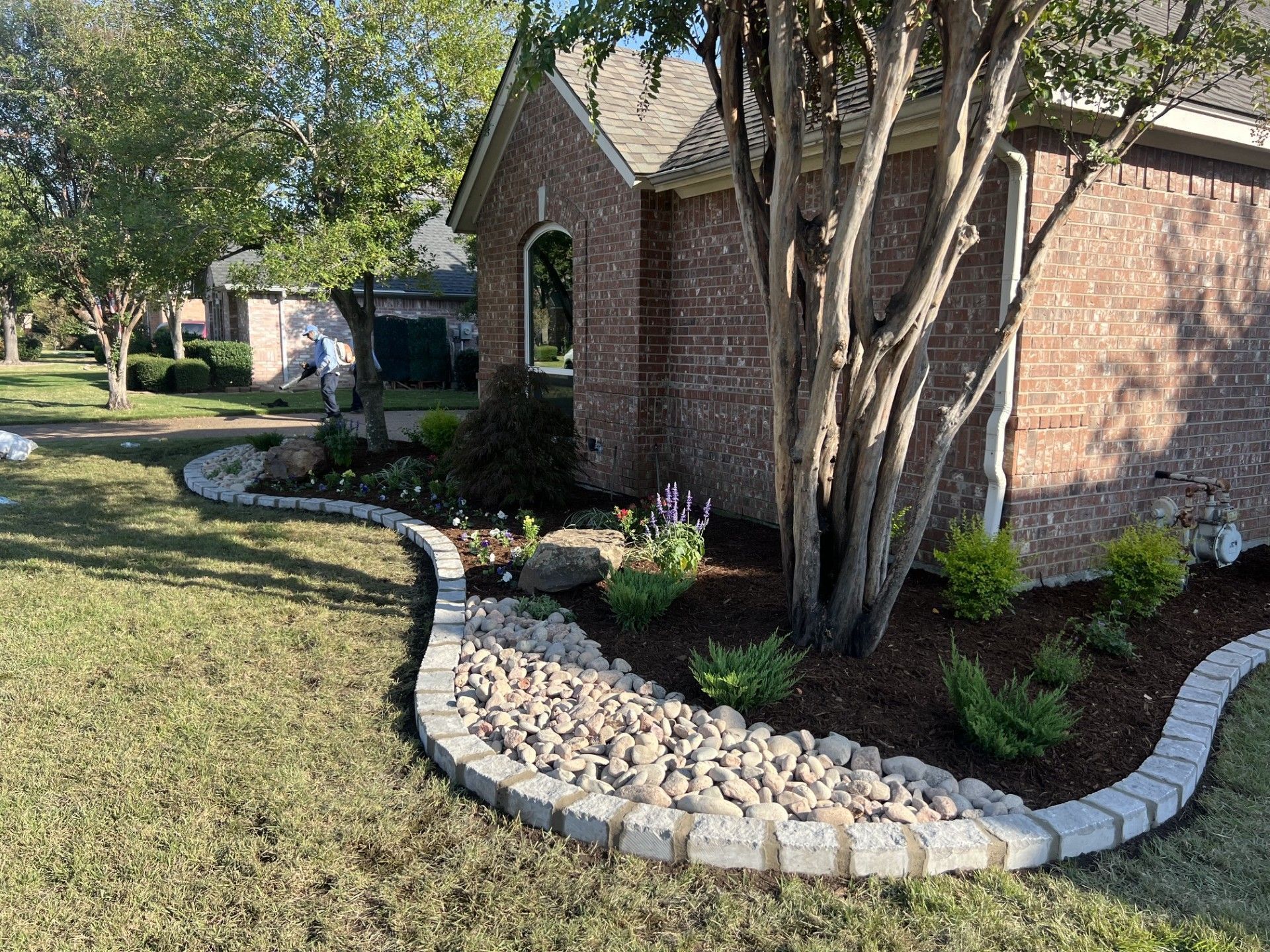 Brick house with curved stone border, landscaped garden bed, and trees in front yard