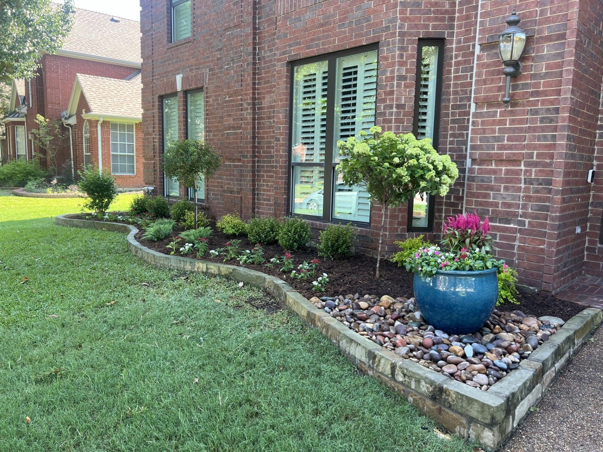 Brick townhouse front yard with curved flower bed, blue planter, and green lawn