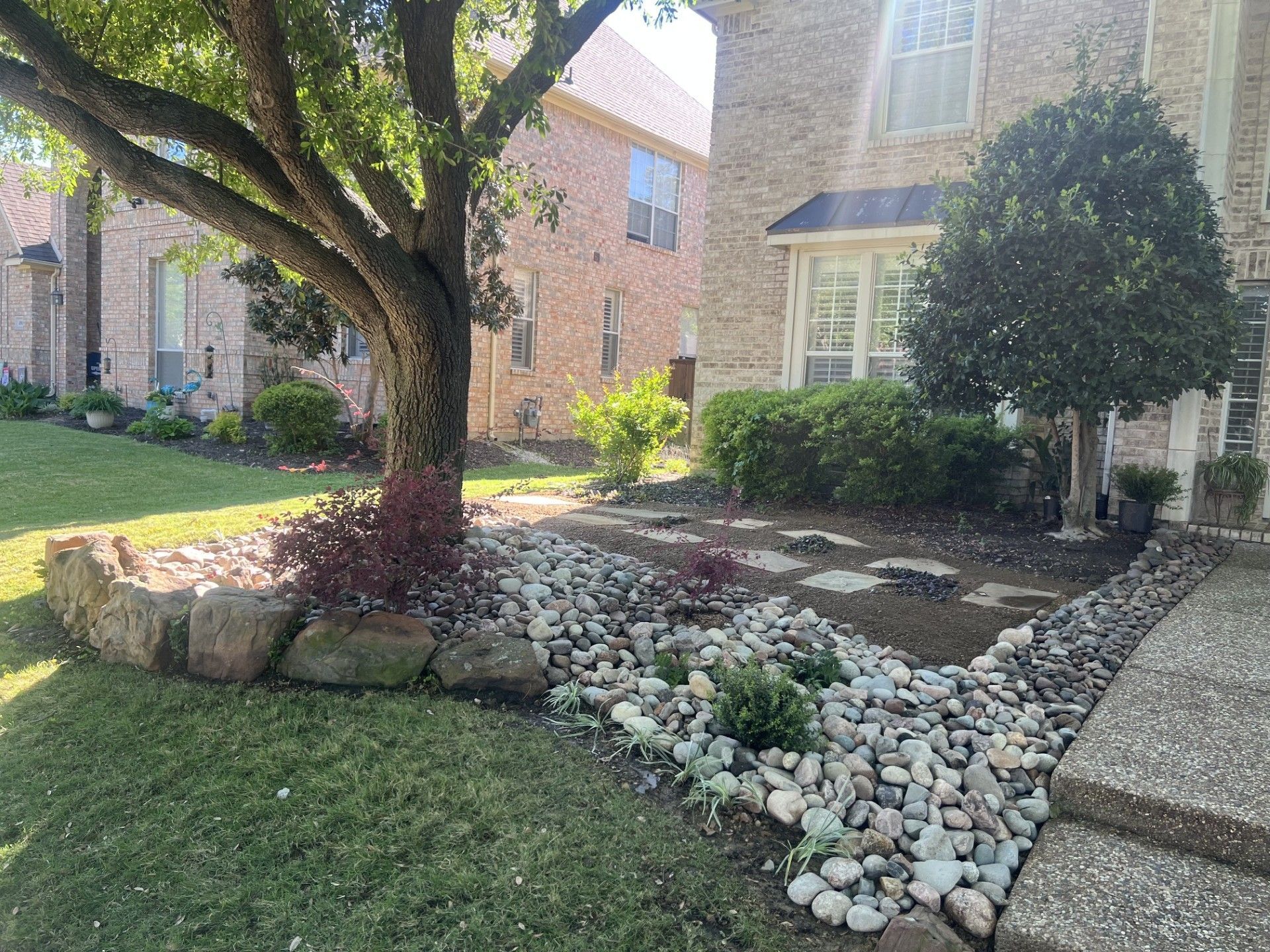 Brick house front yard with large tree, stone edging, and white rock landscaping.