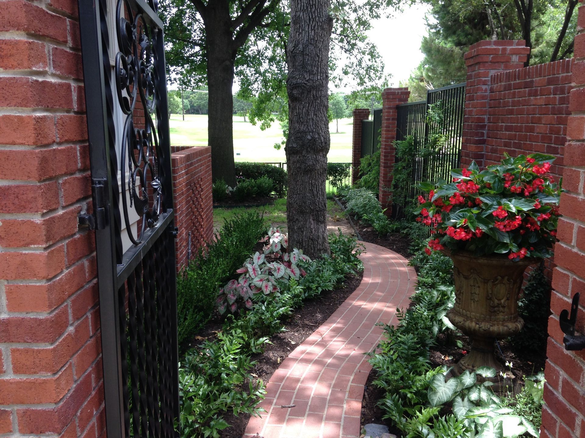 Brick garden path lined with flowers and brick walls beneath trees