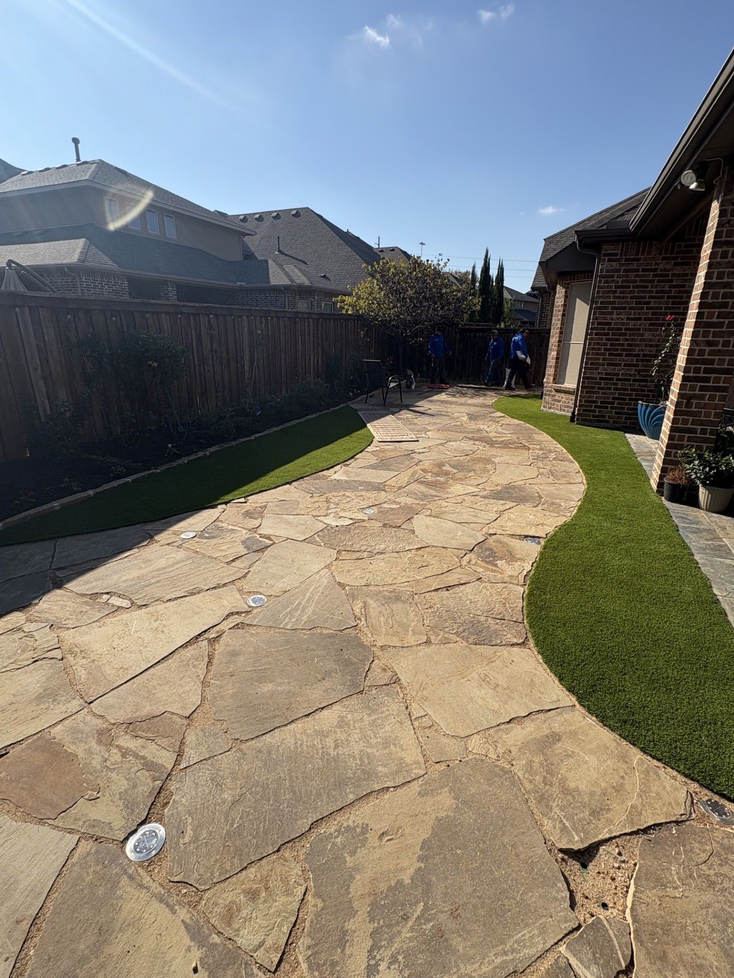 Stone path between houses and a wooden fence in a sunny residential backyard.