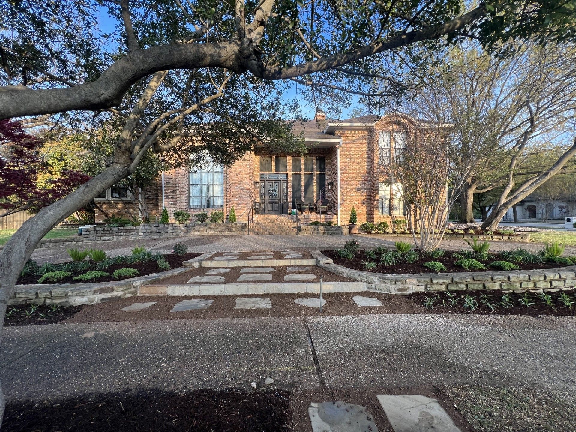 Brick house with a front garden, stone path, and large tree branches overhead
