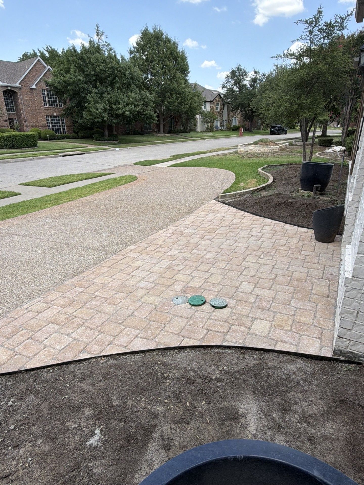 Brick walkway in a suburban neighborhood, with a pair of green sandals on the path and houses in the background.