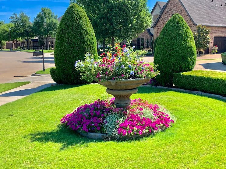 Decorative flower urn in a manicured suburban yard with bright pink blooms and trimmed evergreens