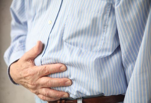 Hand holding lower abdomen of a blue striped shirt, suggesting stomach pain or discomfort