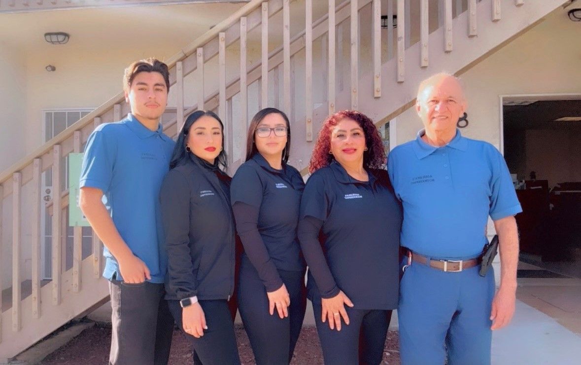 Five people in blue and black uniforms stand outside, posing for a photo in front of a building with stairs.
