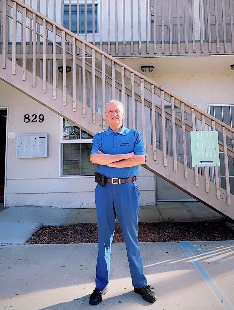 Man in blue uniform stands in front of a building with stairs, arms crossed. Building number 829.