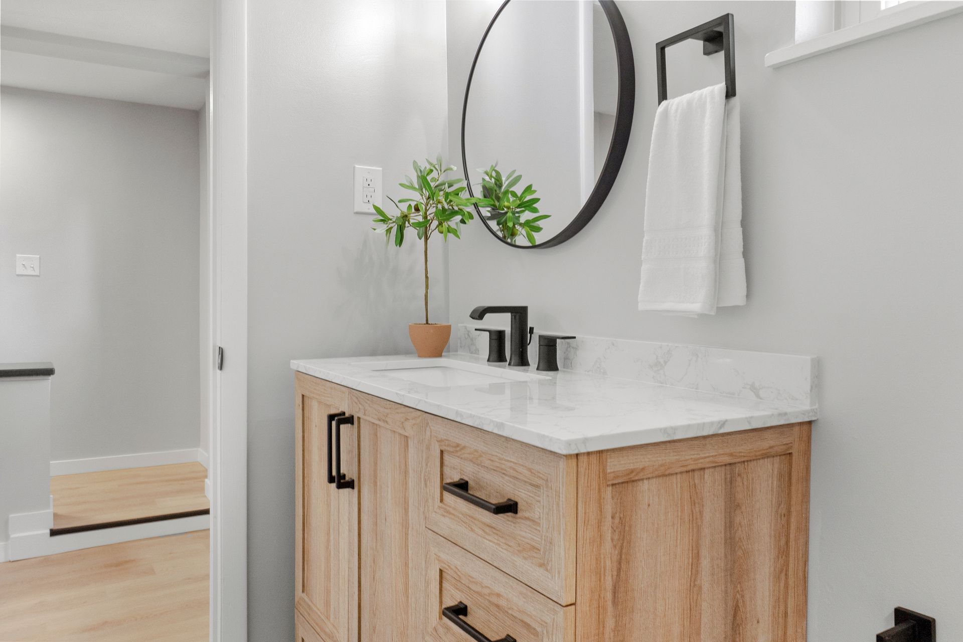 Bathroom with wooden vanity, round mirror, and black fixtures. A towel hangs on the wall.
