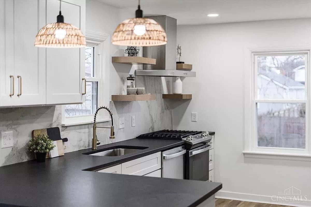 Modern kitchen with white cabinets, dark countertops, gold fixtures, and woven pendant lights.