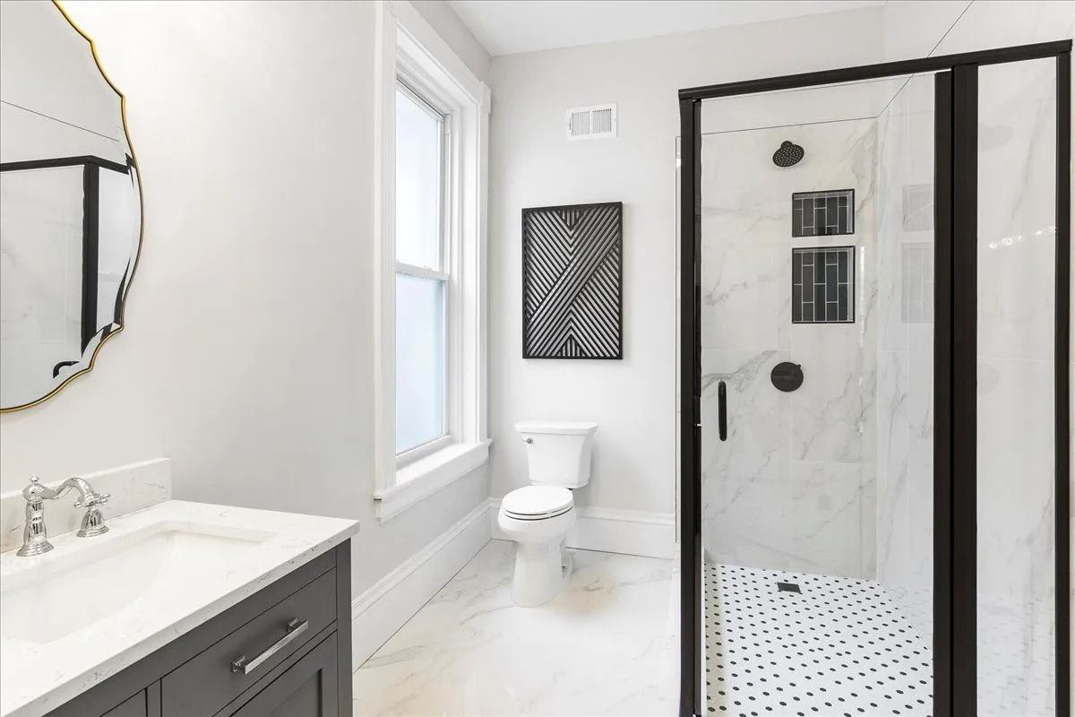 Modern bathroom with marble shower and flooring, black accents, and a vanity.