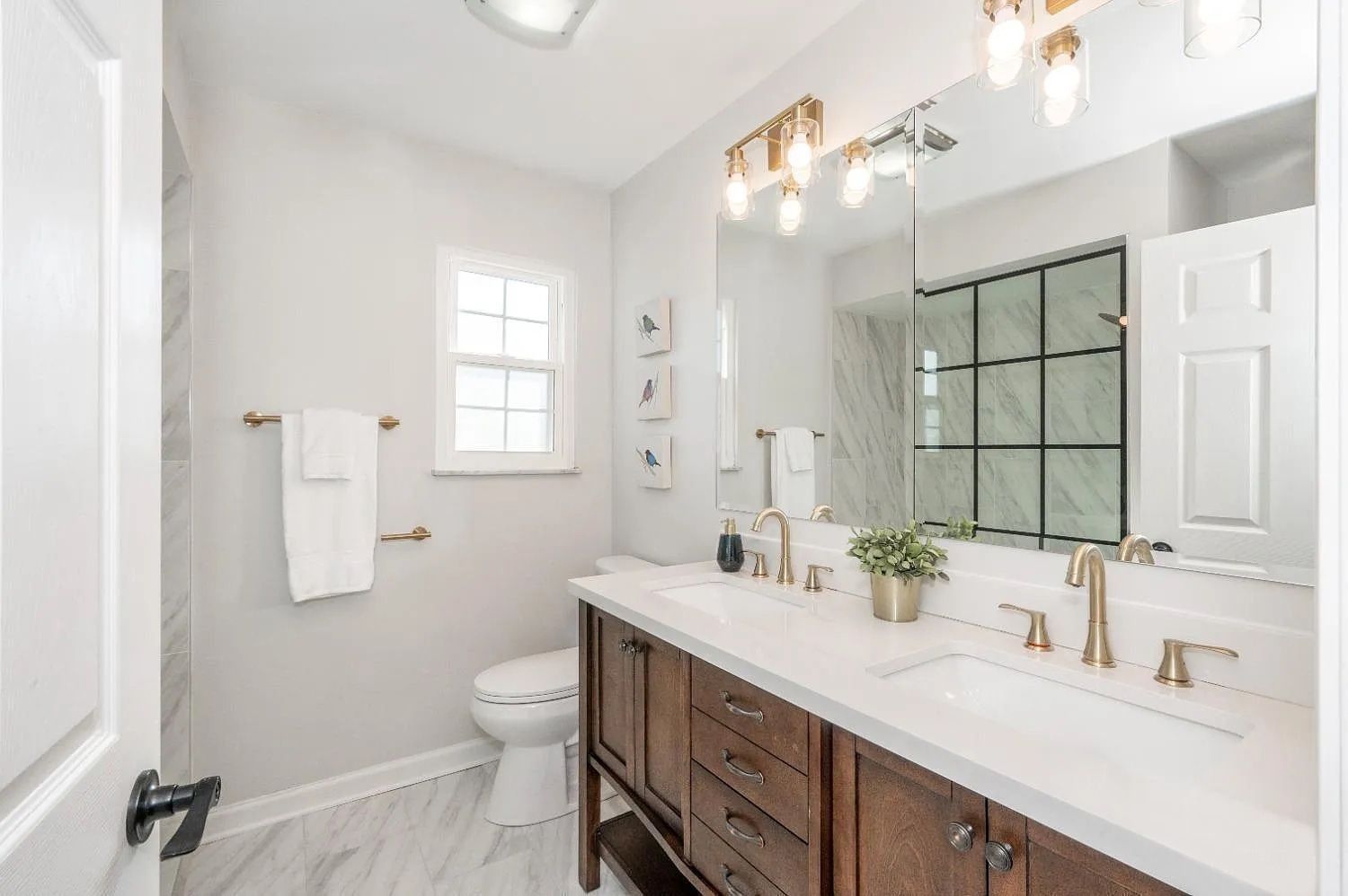 Bathroom with a wooden vanity, marble countertop, and gold fixtures. Features a shower with black grid accents.