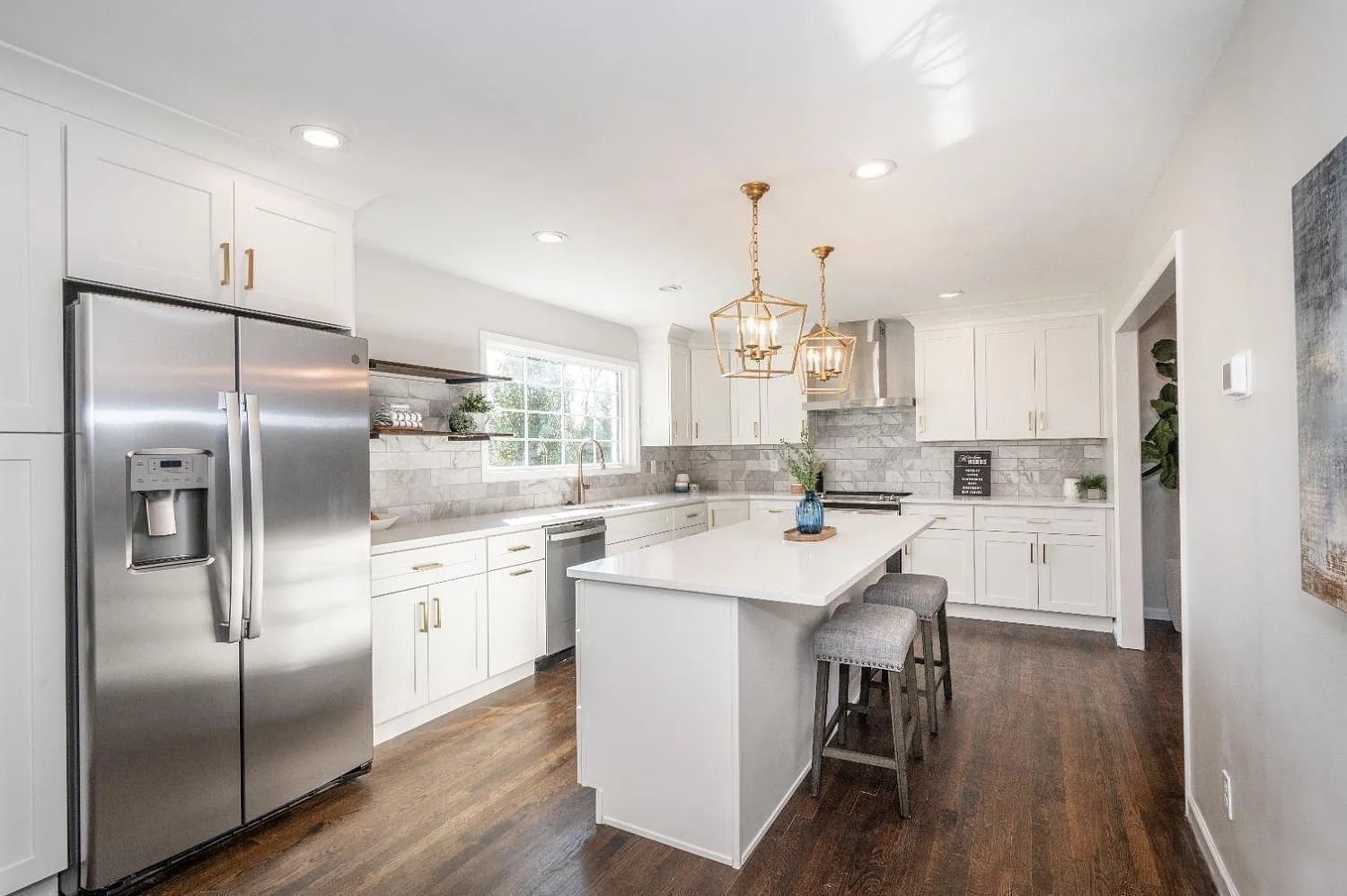 Modern white kitchen with stainless steel appliances, dark wood floors, and island with seating.