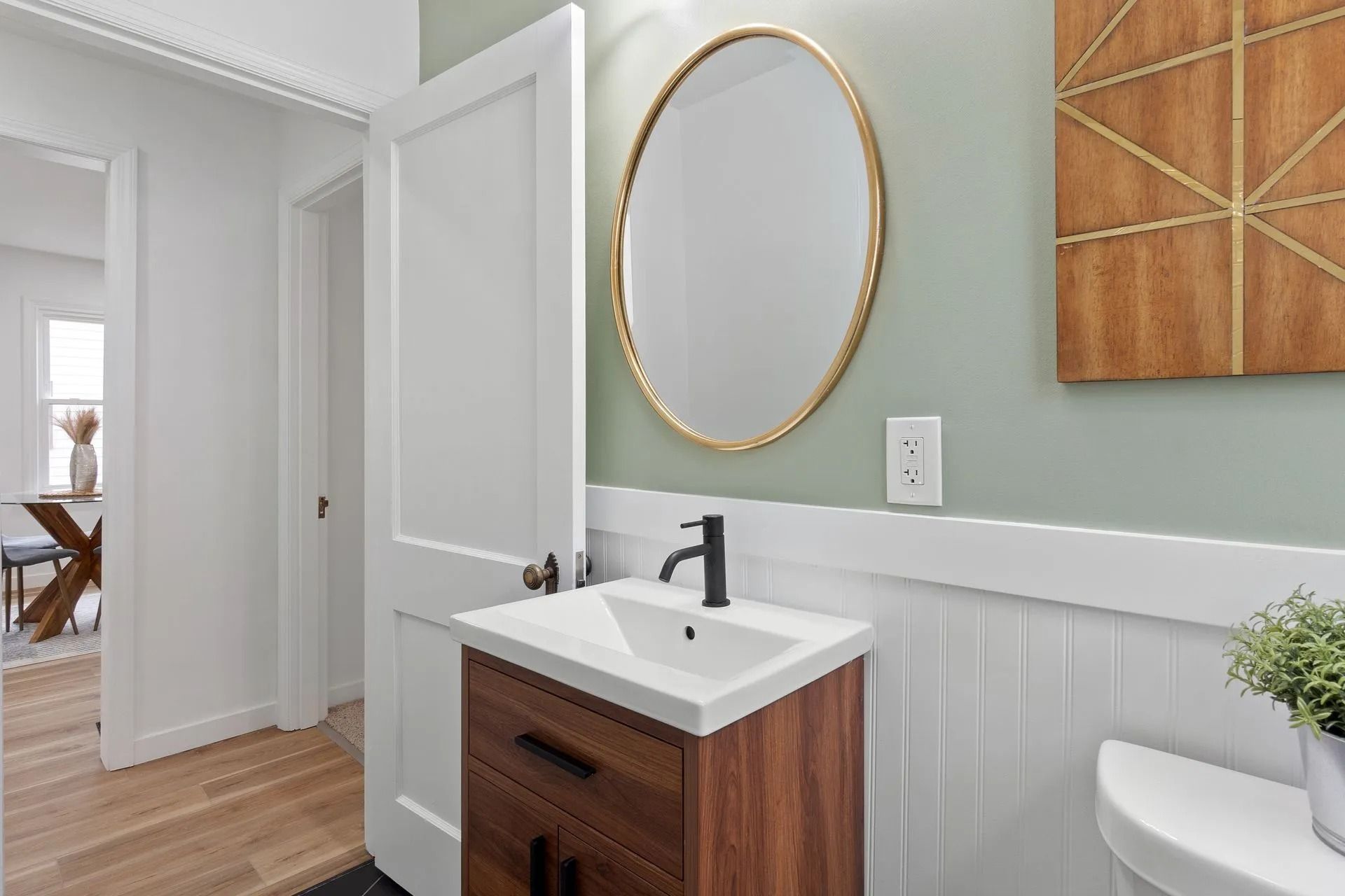 Bathroom with wooden vanity, oval mirror, and light green wall.