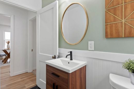 Bathroom with a wooden vanity, oval mirror, and sage green wall. White beadboard wainscoting and gold accent.