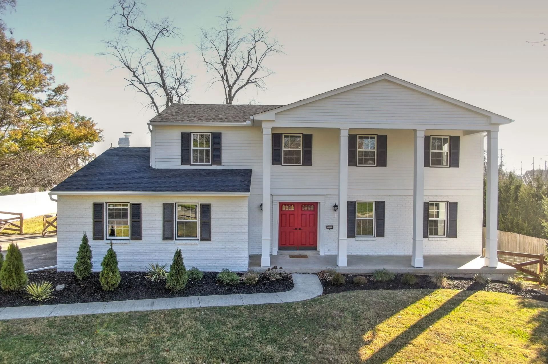 White two-story house with black shutters and red front door. Columns support the front porch.