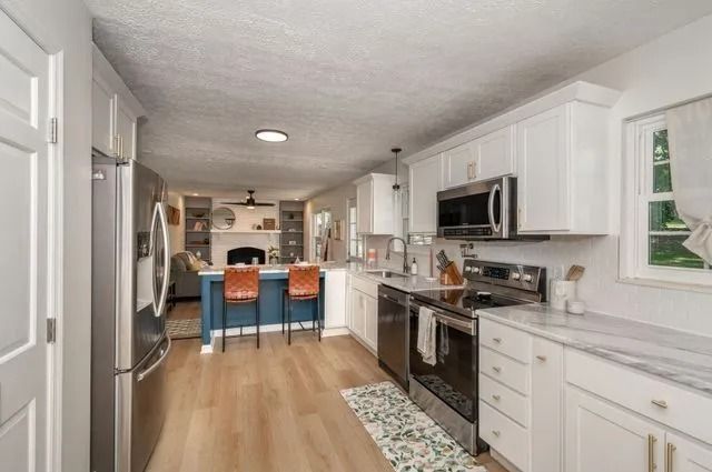 Kitchen with white cabinets, stainless steel appliances, and blue island with bar stools.