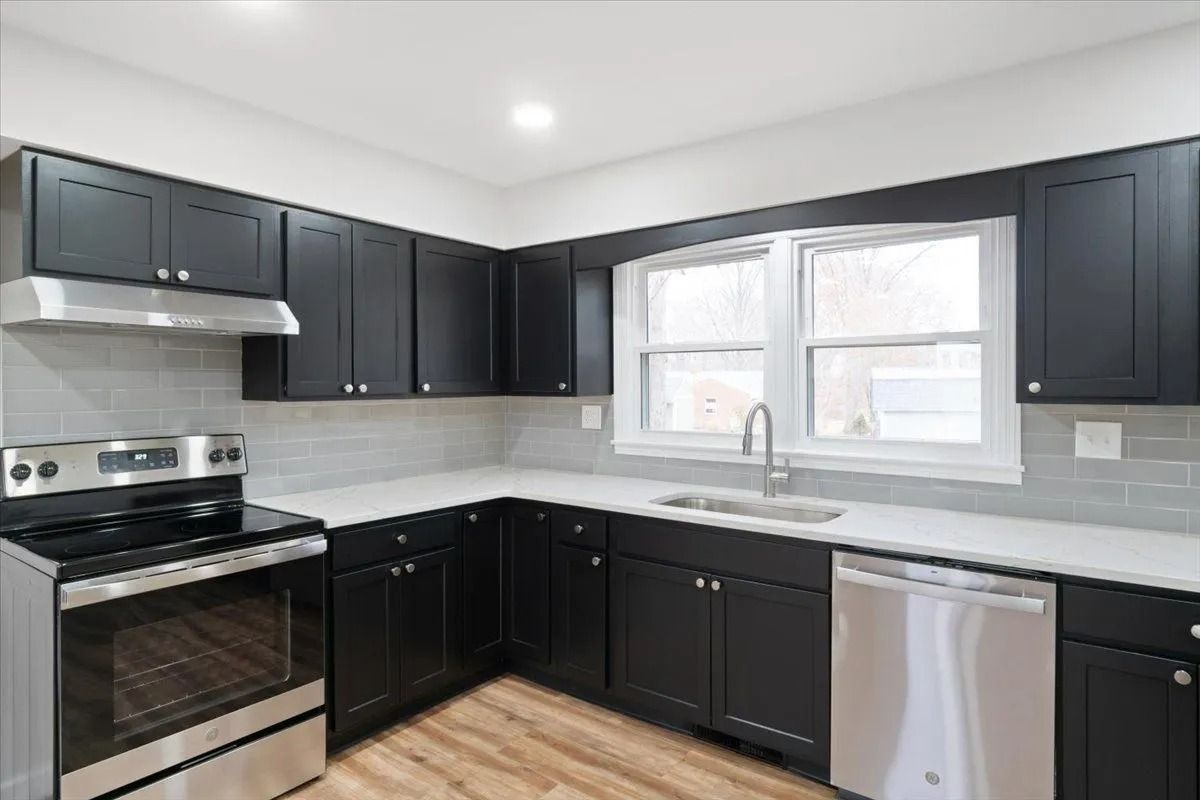 Kitchen with black cabinets, stainless steel appliances, white countertops, and a window above the sink.