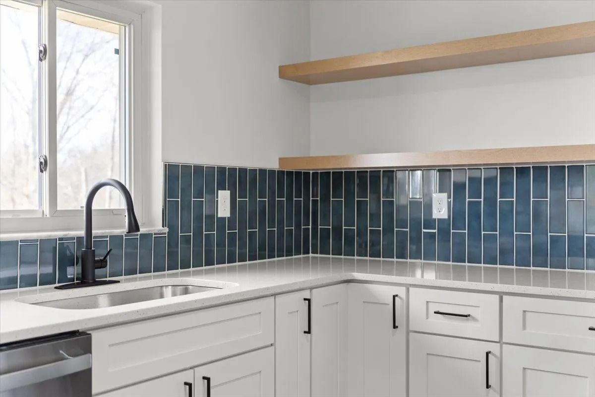 Modern kitchen with white cabinets, blue tile backsplash, stainless steel sink, and wooden shelf.