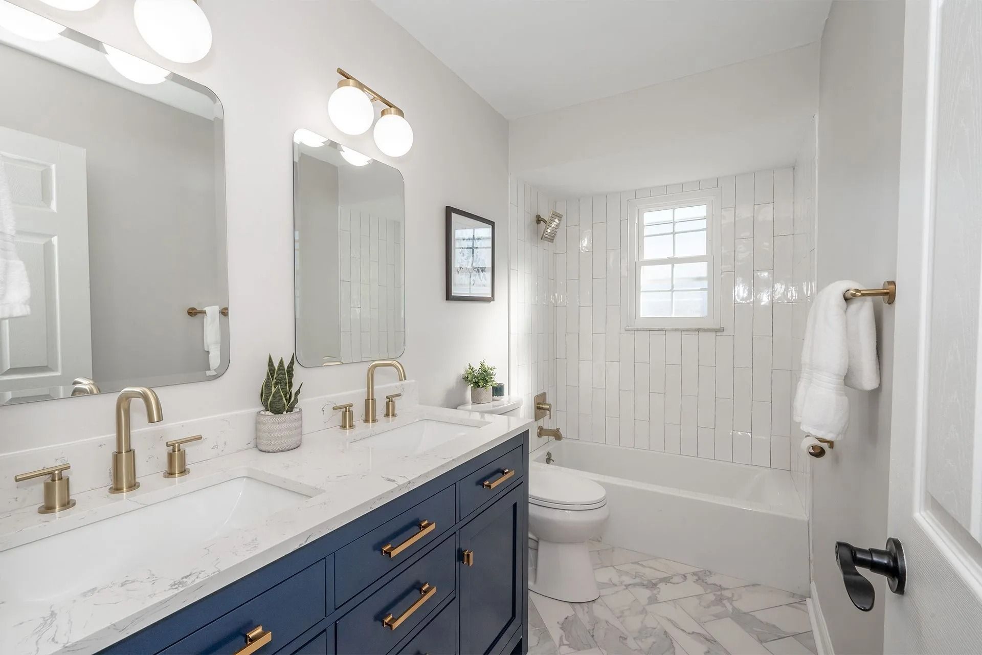 Modern bathroom with blue vanity, gold fixtures, and white marble tile.