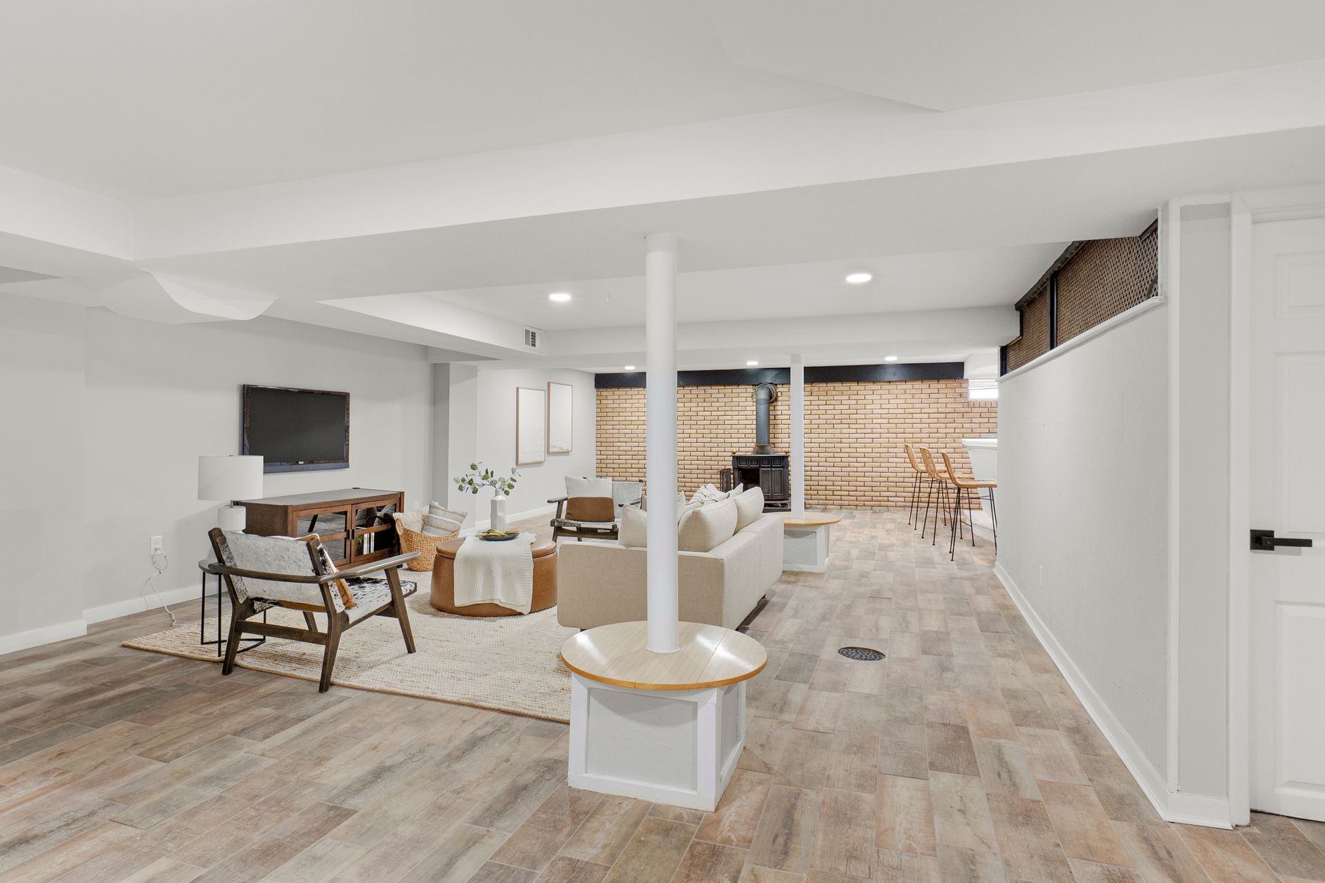 Bright, modern basement living area with wood flooring, white walls, and a central support column.