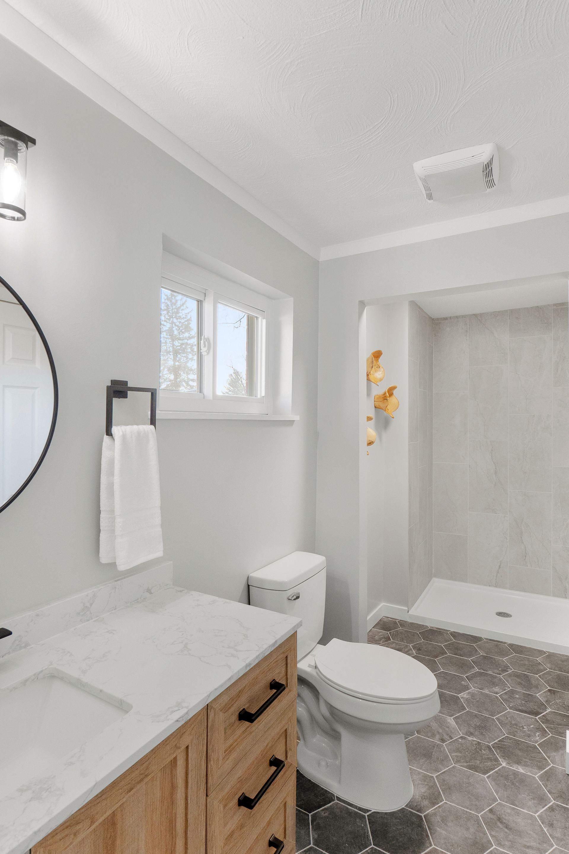Bathroom with light gray walls, white countertop, wooden vanity, and hexagonal tiled floor.