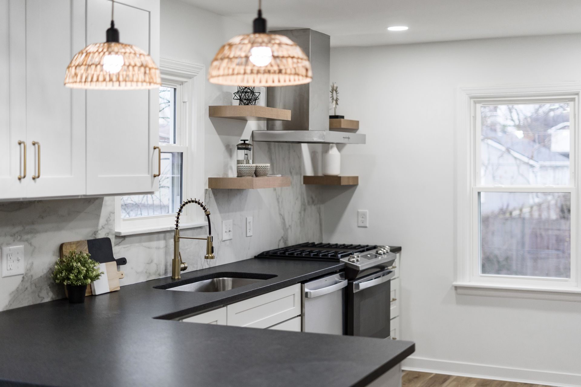 Modern kitchen with white cabinets, black countertop, open shelves, and rattan pendant lights.