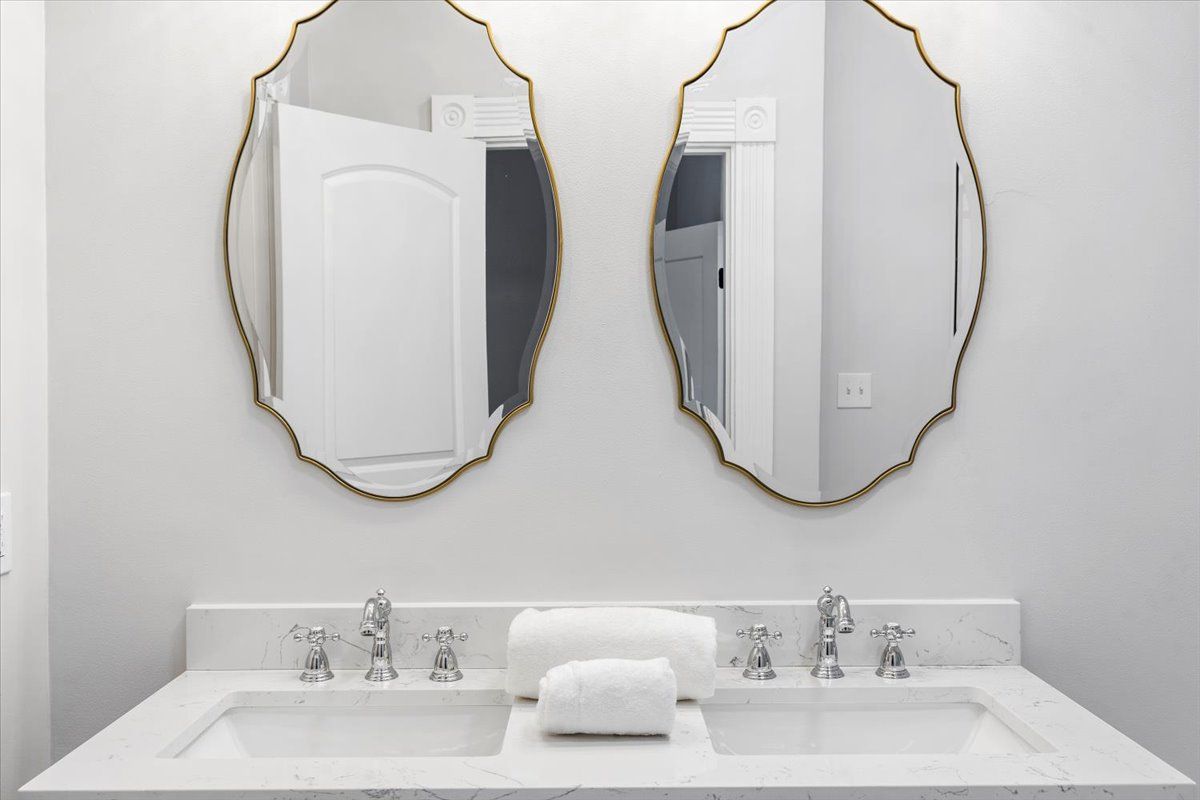Bathroom vanity with two sinks, gold-framed mirrors, and white countertop.