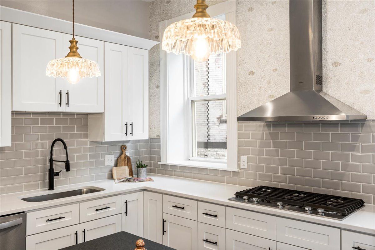 White kitchen with light cabinets, gray backsplash, and two decorative light fixtures.